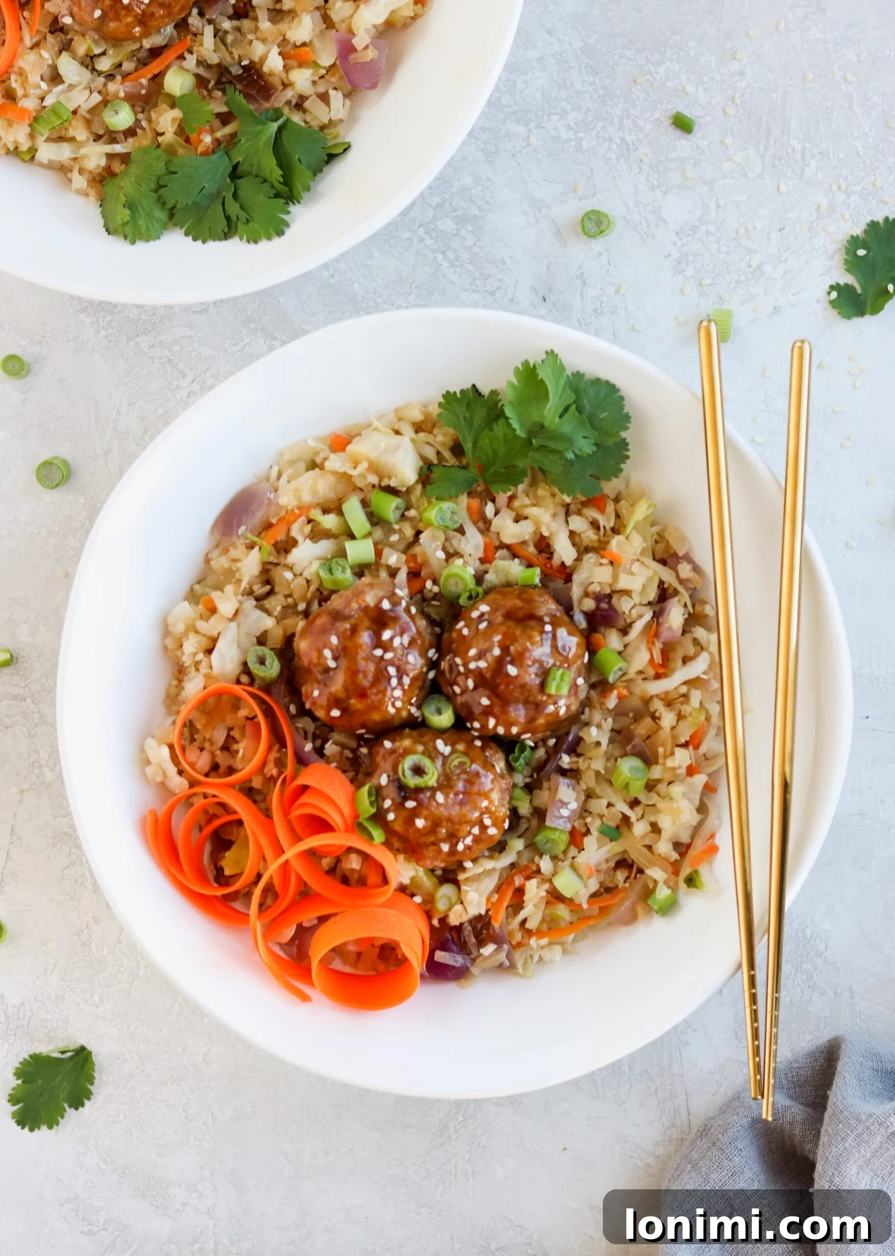 A bowl of Asian Pork Meatball Bowls, showcasing the glazed meatballs, cauliflower fried rice, and vibrant garnishes.
