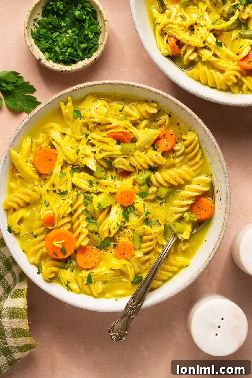 Two steaming bowls of homemade gluten-free chicken soup, featuring chunks of tender chicken, vibrant carrots, and gluten-free noodles, garnished with fresh herbs.
