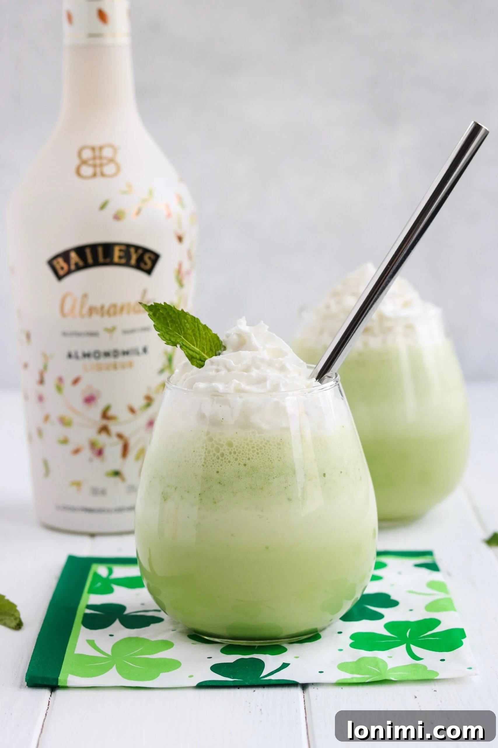 Two glasses of Spiked Shamrock Shake, garnished with whipped cream, in front of a green backdrop.