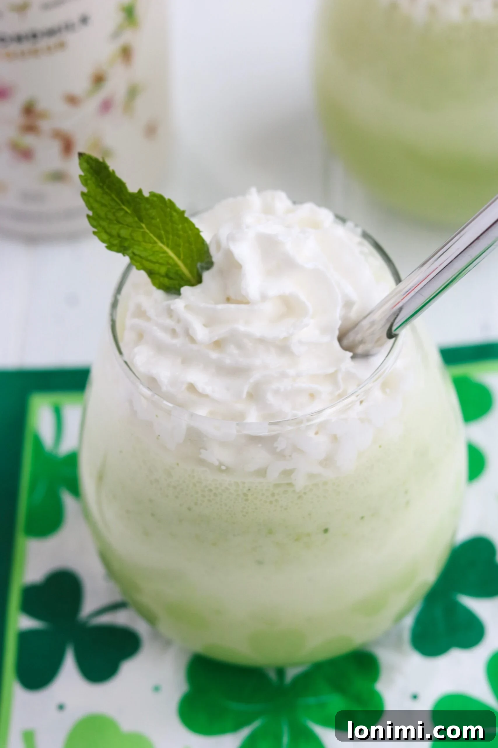 Close-up of a Spiked Shamrock Shake, garnished with whipped cream and green sprinkles, with a festive background.