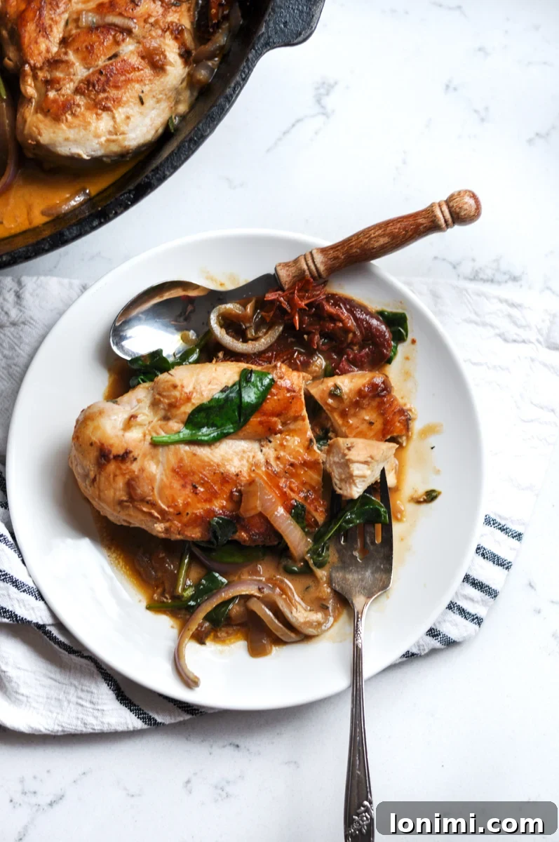 Close-up of a serving of Creamy Tuscan Chicken Skillet, showing the texture of the chicken, spinach, and the rich sauce, topped with fresh basil leaves.