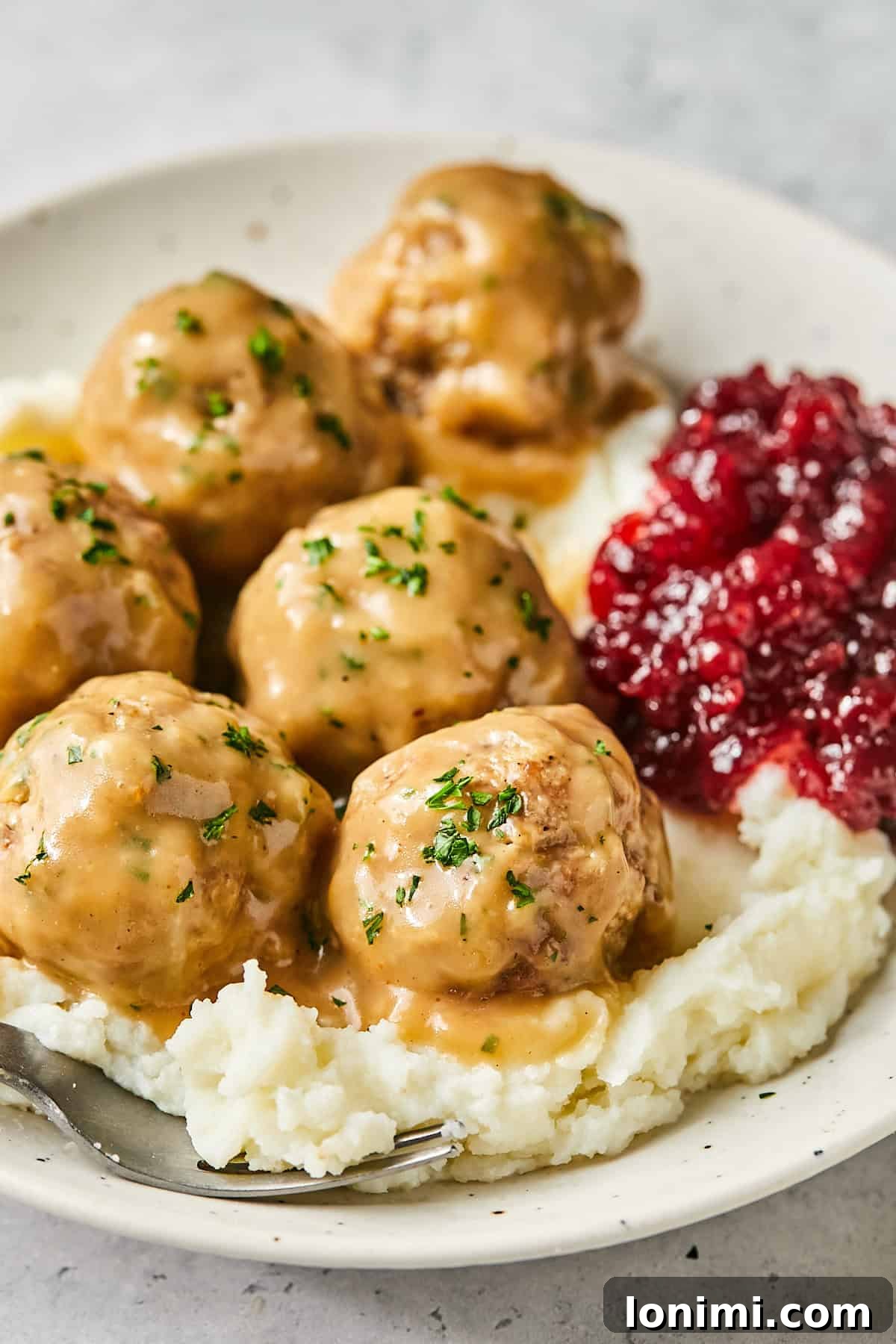 Swedish meatballs in a bowl with creamy gravy and lingonberry jam, served over mashed potatoes for a comforting meal.
