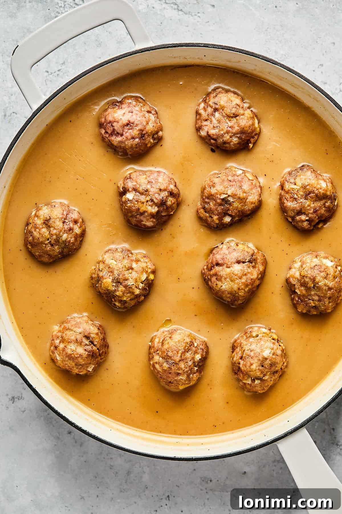 Baked Swedish meatballs gently simmering in the rich, creamy dairy-free gravy in a frying pan, garnished with fresh parsley.