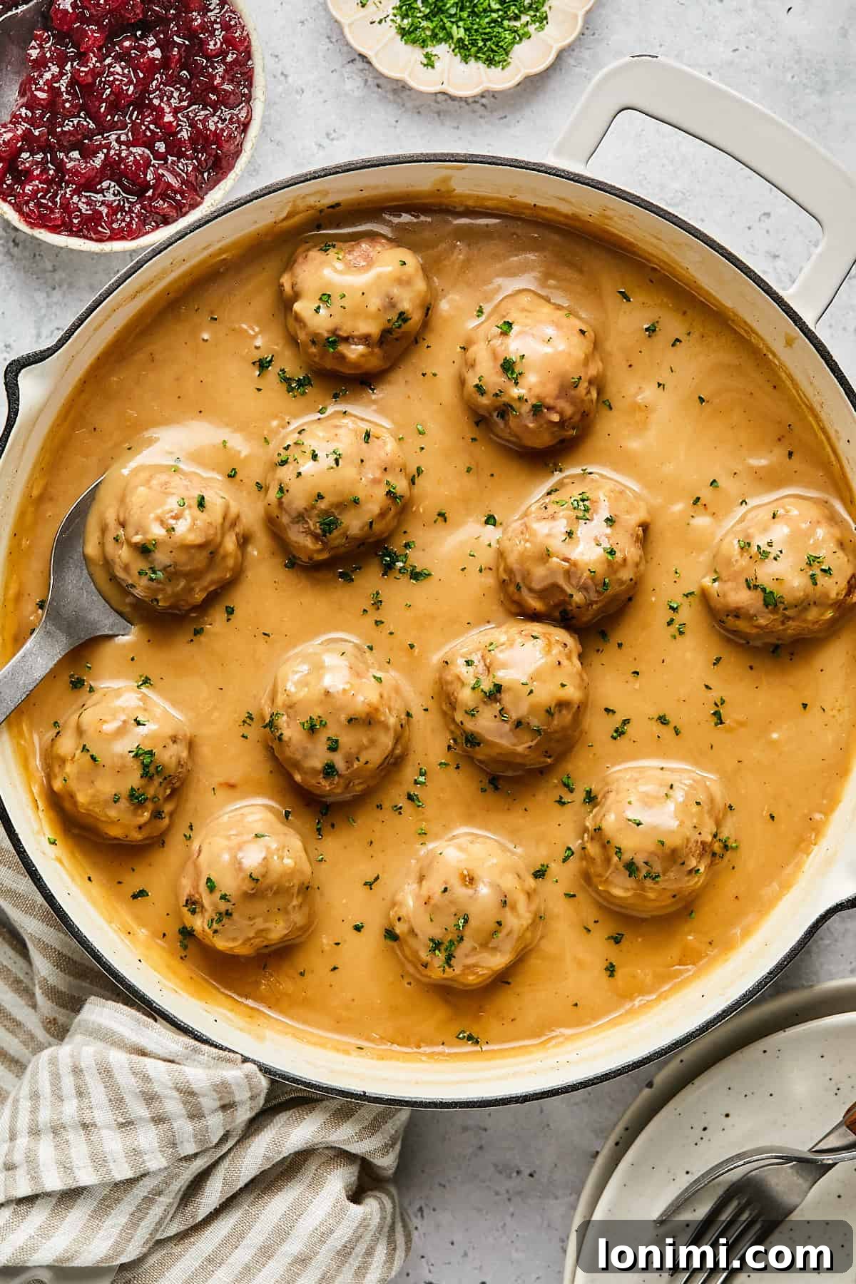 Close-up of baked Swedish meatballs generously coated in creamy gravy, garnished with fresh parsley in a large pan.