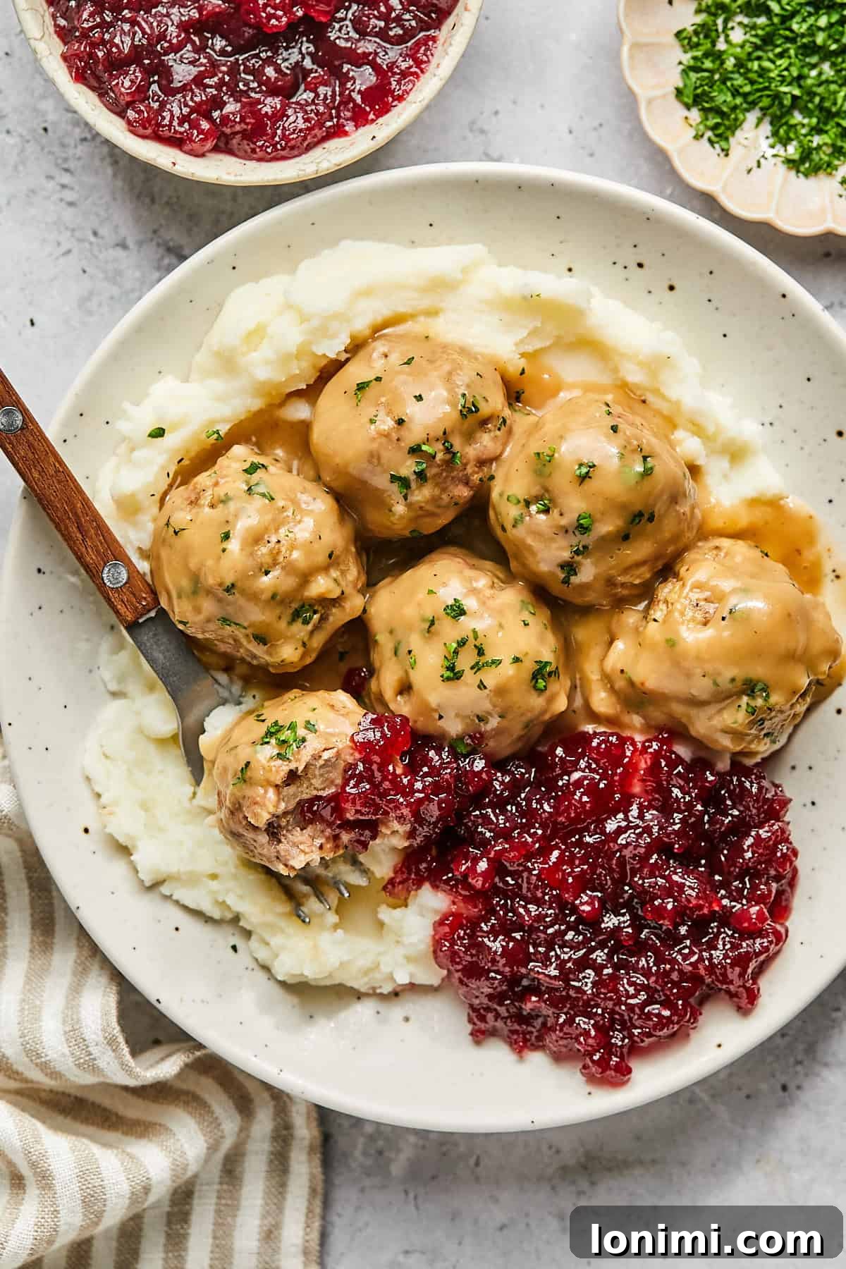 A bowl of gluten-free Swedish meatballs, mashed potatoes, and a side of traditional lingonberry jam, ready for a cozy meal.