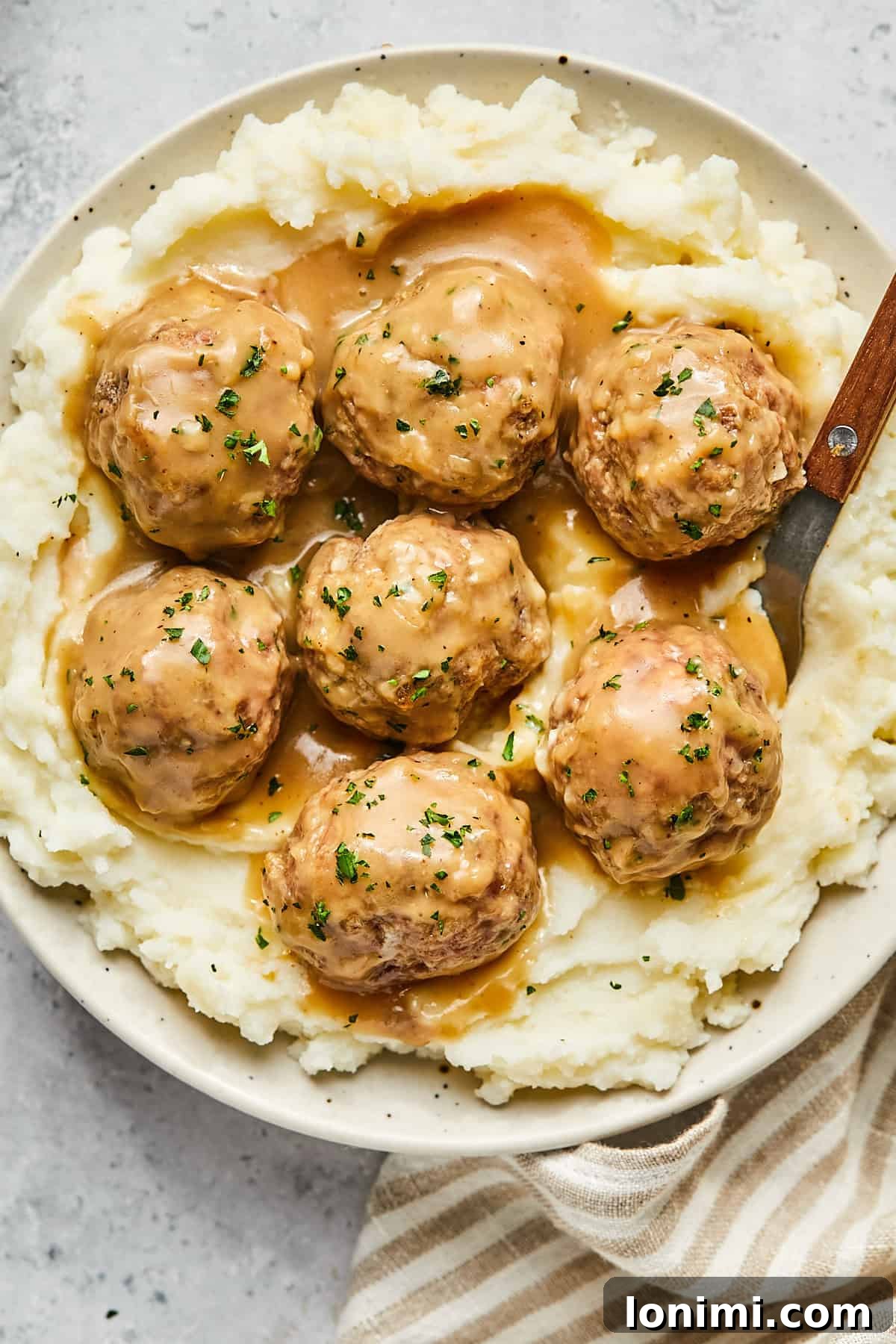 A serving of creamy Swedish meatballs in a bowl, generously topped with fresh parsley for garnish.