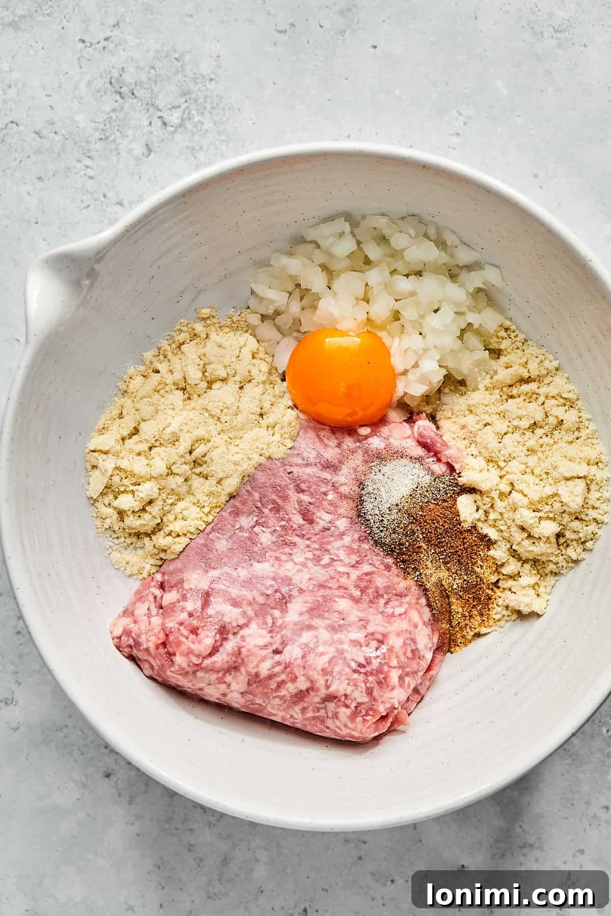 Raw ingredients for pork meatballs mixed in a large glass bowl, ready for shaping.