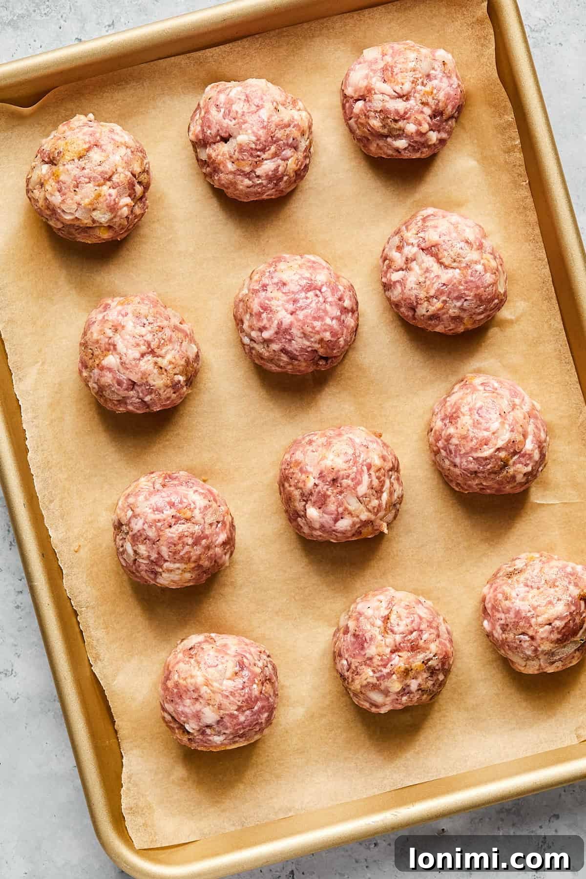 Evenly shaped raw meatballs neatly arranged on a parchment-lined baking sheet, ready for baking.