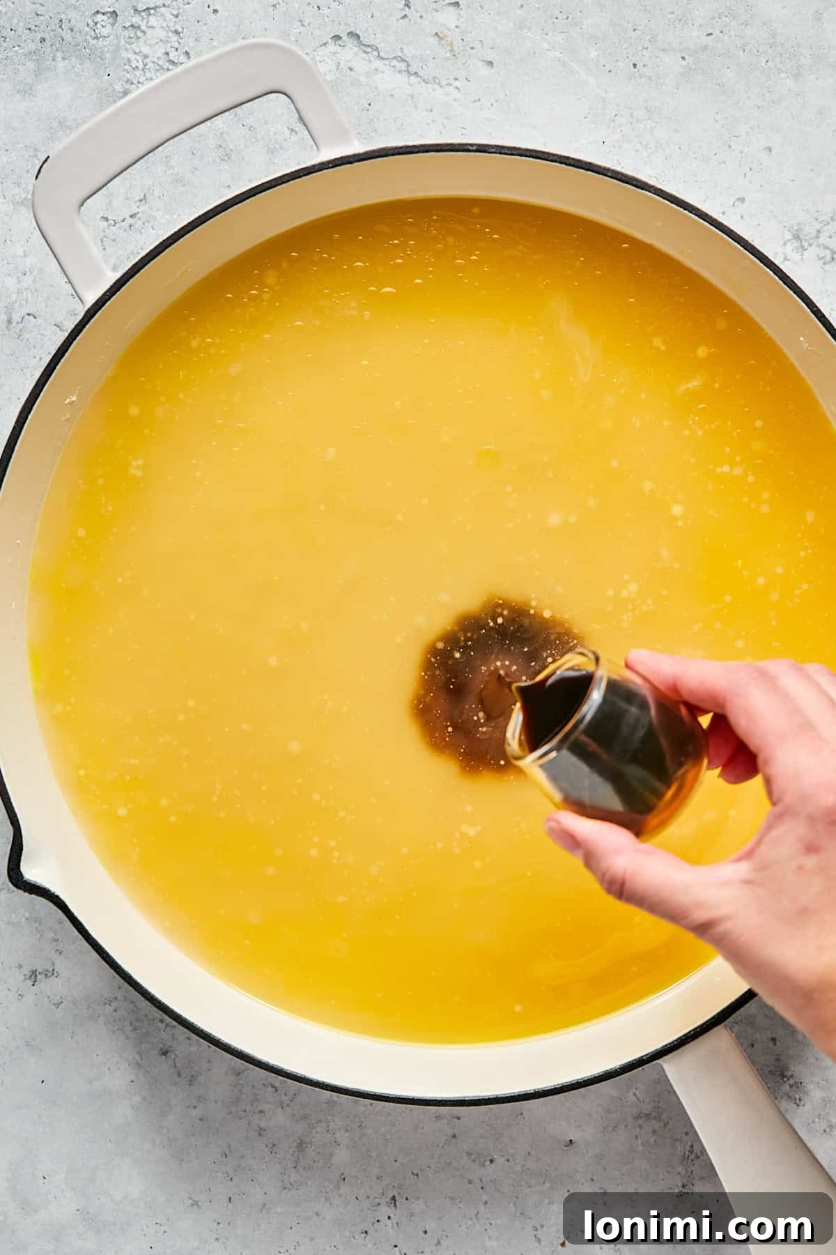 Chicken broth and coconut aminos being added to the roux in a pan, ready to be whisked into a smooth gravy.