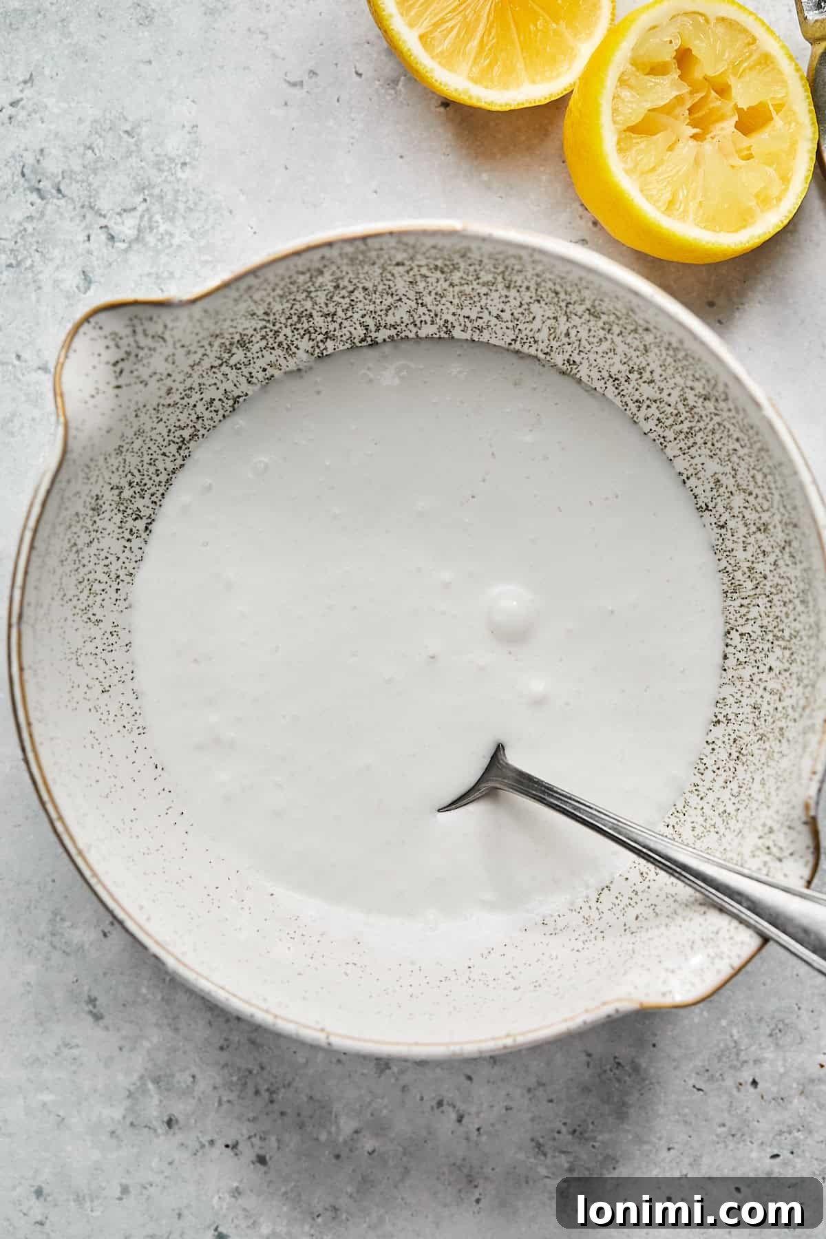 Dairy-free sour cream alternative, made from coconut cream and lemon juice, in a bowl with a spoon and fresh lemons on the side.
