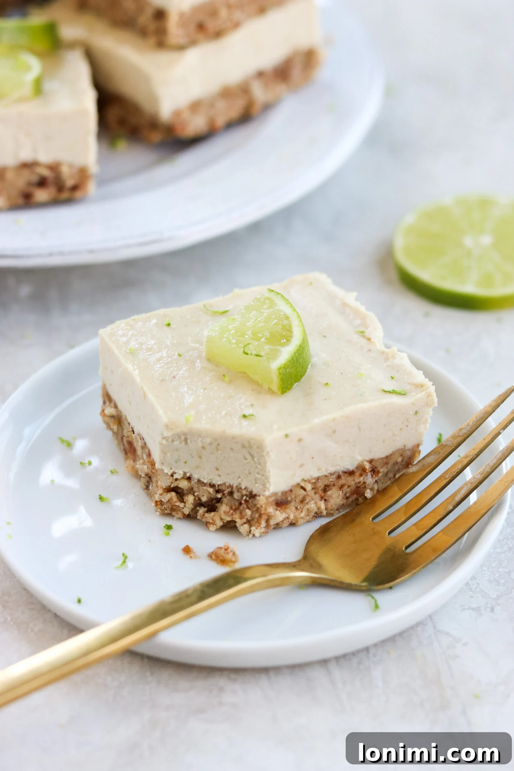 A single vegan key lime cheesecake bar elegantly placed on a small white plate with a gold fork.