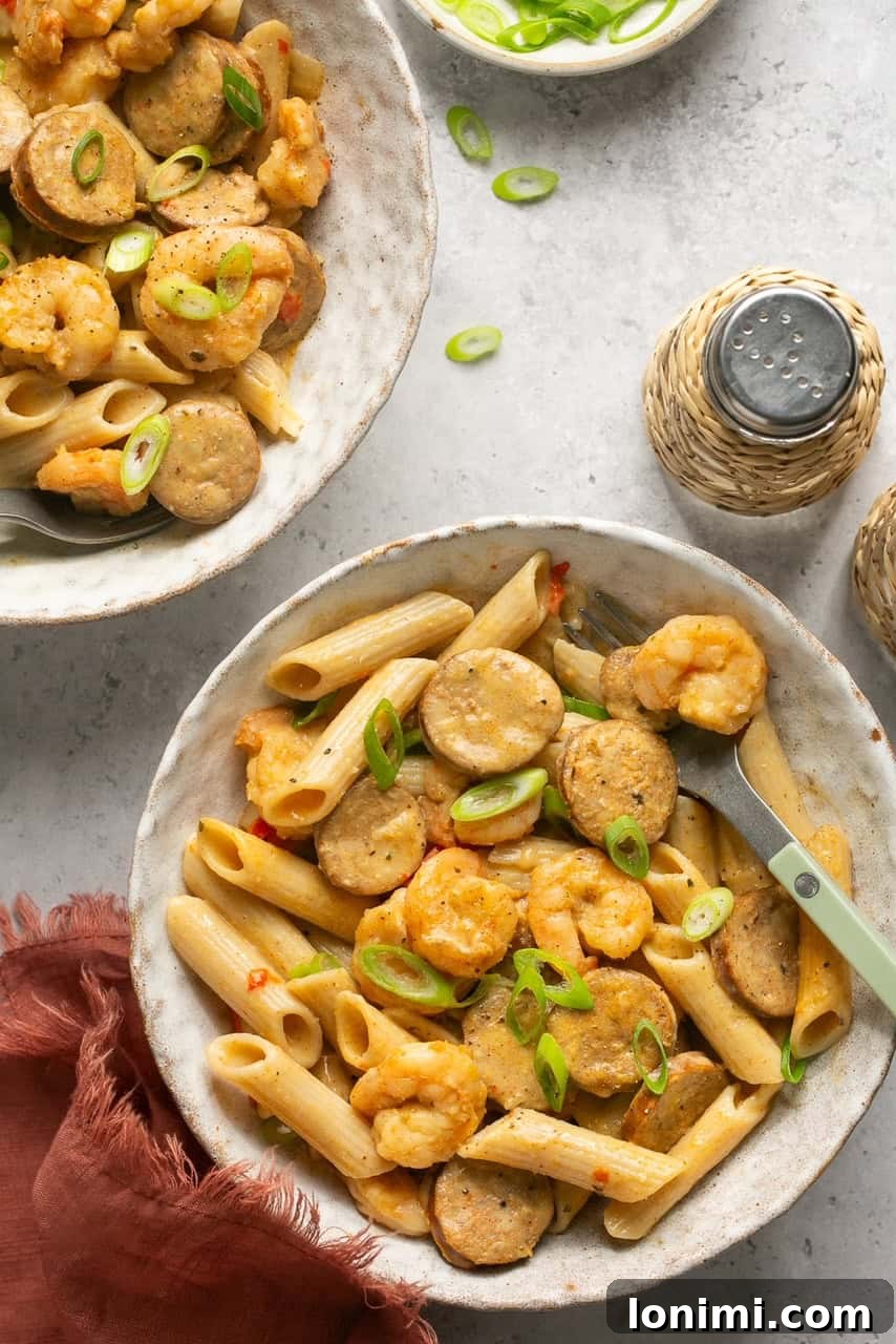 Two bowls of creamy gluten-free cajun shrimp and sausage pasta topped with fresh green onions
