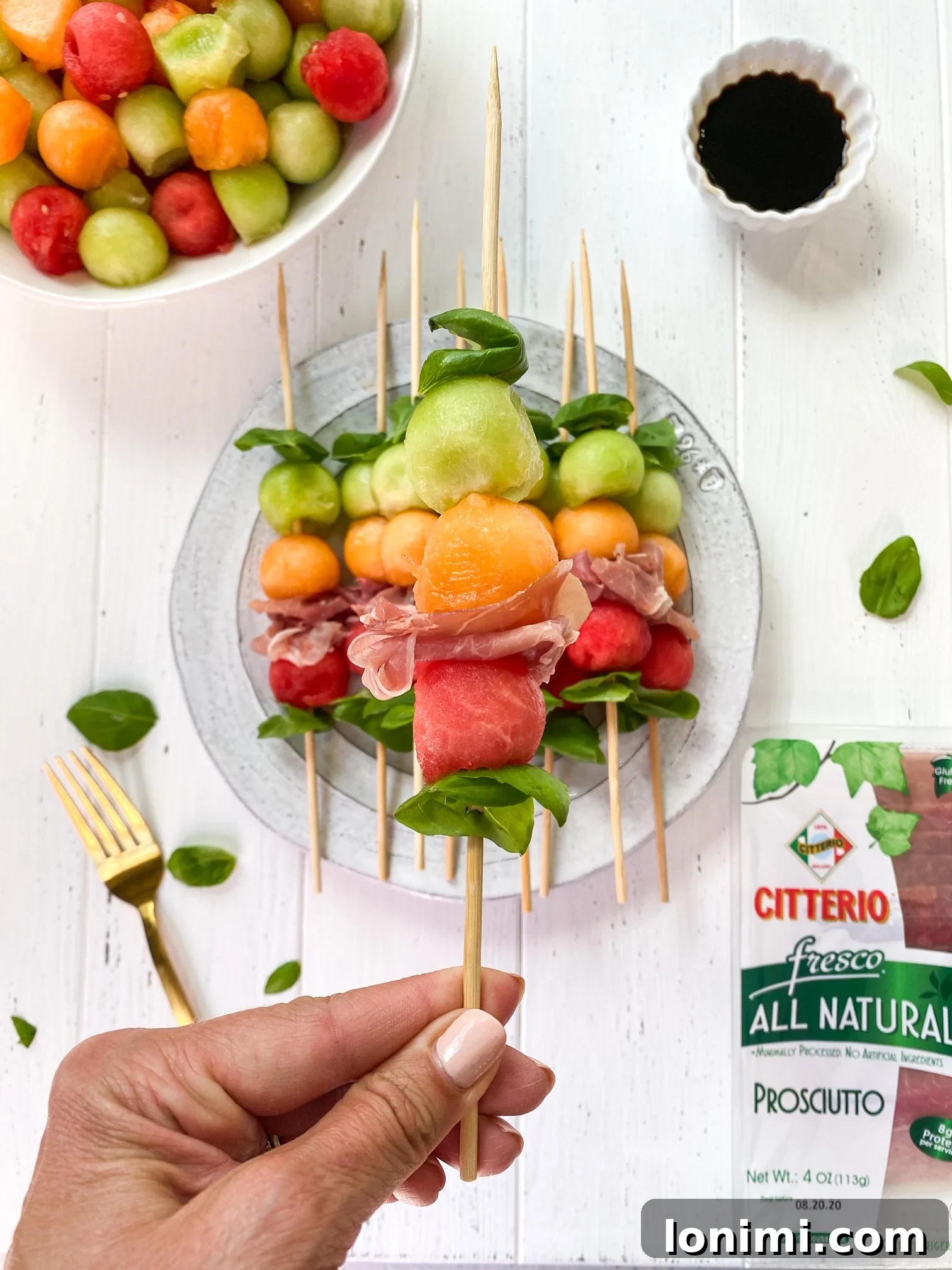 Close-up of a hand reaching for a Melon Basil Prosciutto Skewer from a platter