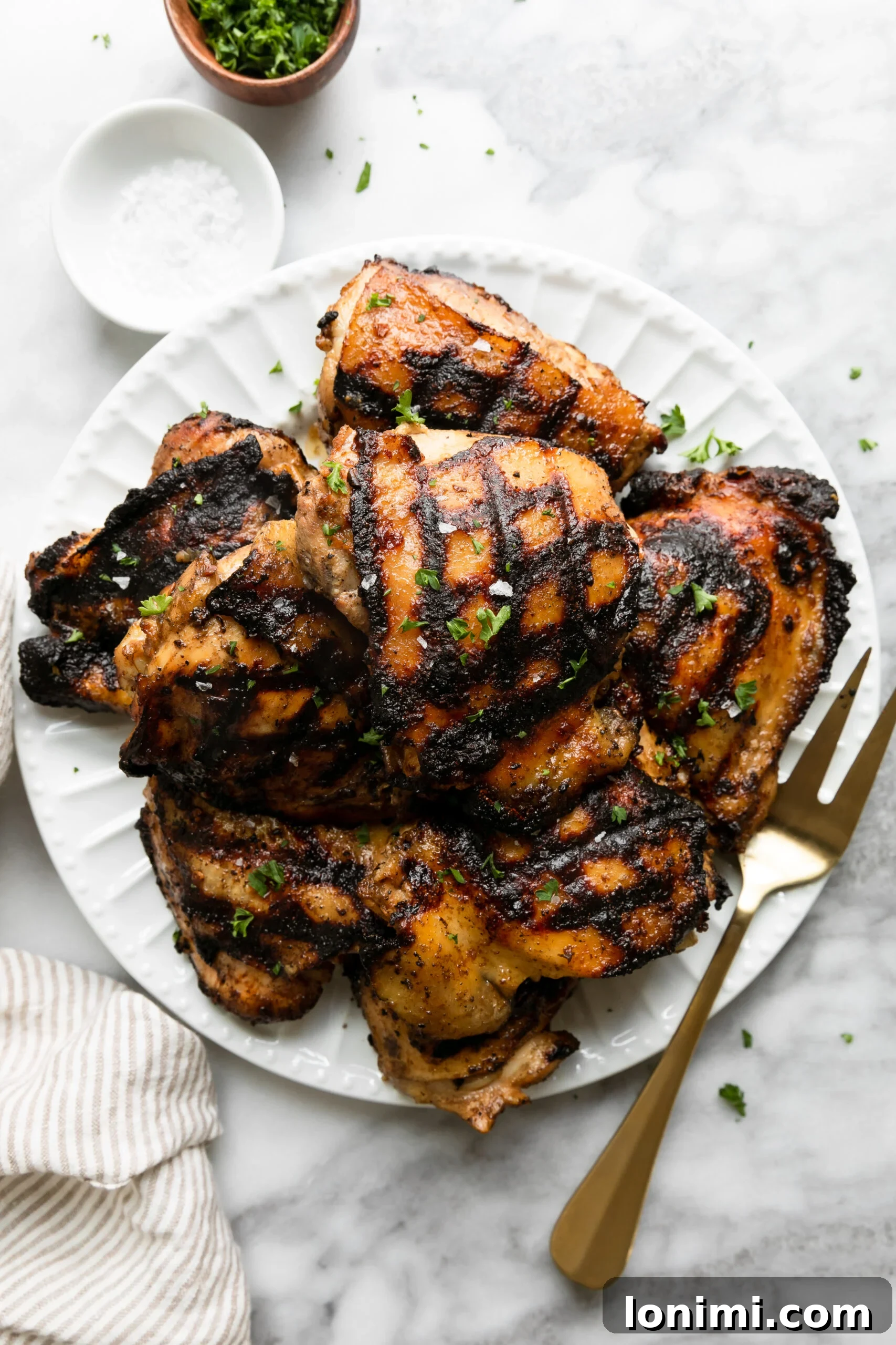 Keto Chicken Thighs Perfectly Marinated for Health and Flavor 2 grilled chicken thighs on a white plate with a gold fork