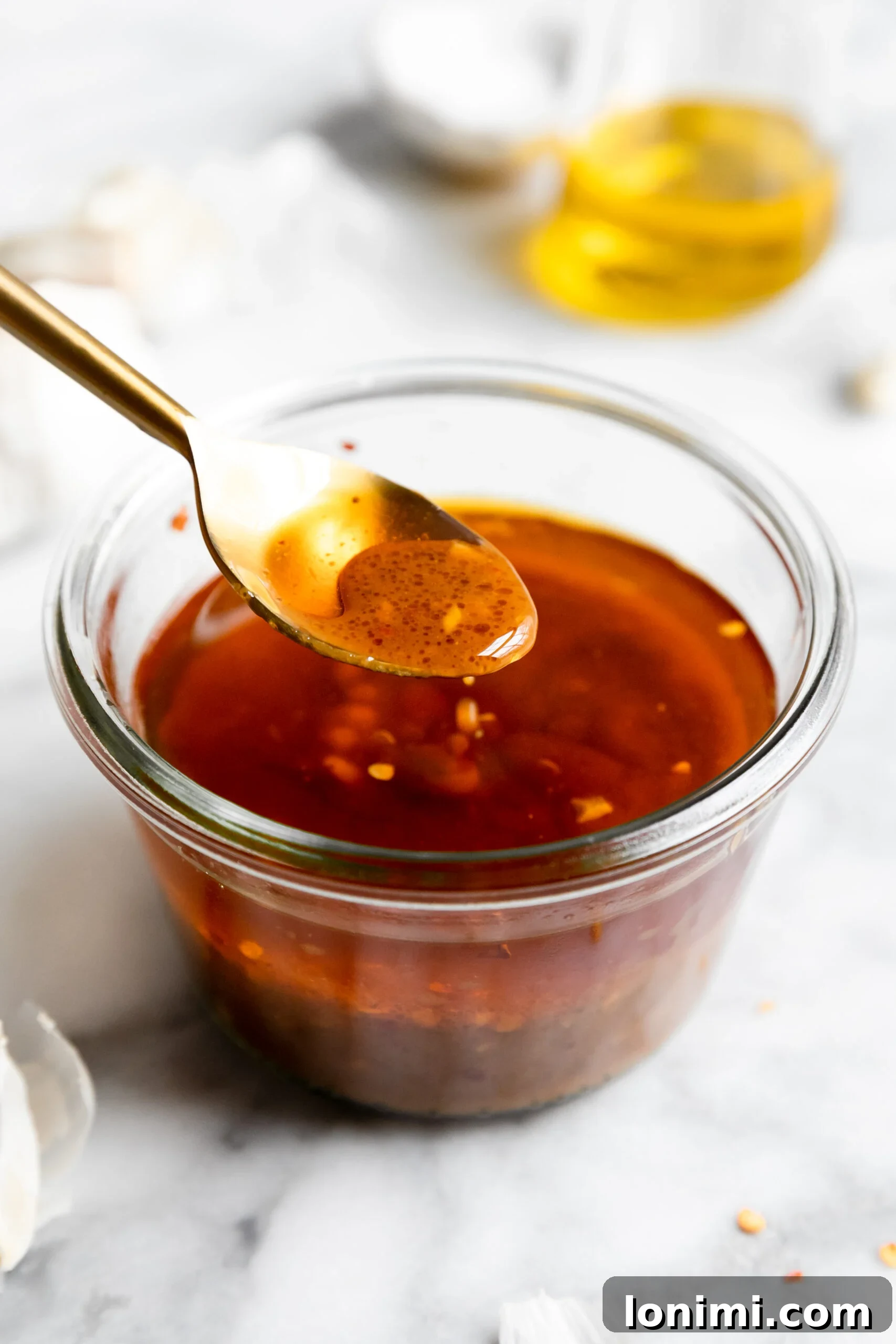 Keto Chicken Thighs Perfectly Marinated for Health and Flavor 4 a closeup of a small jar filled with chicken thigh marinade with a gold spoon showing a closeup of some of the sauce.