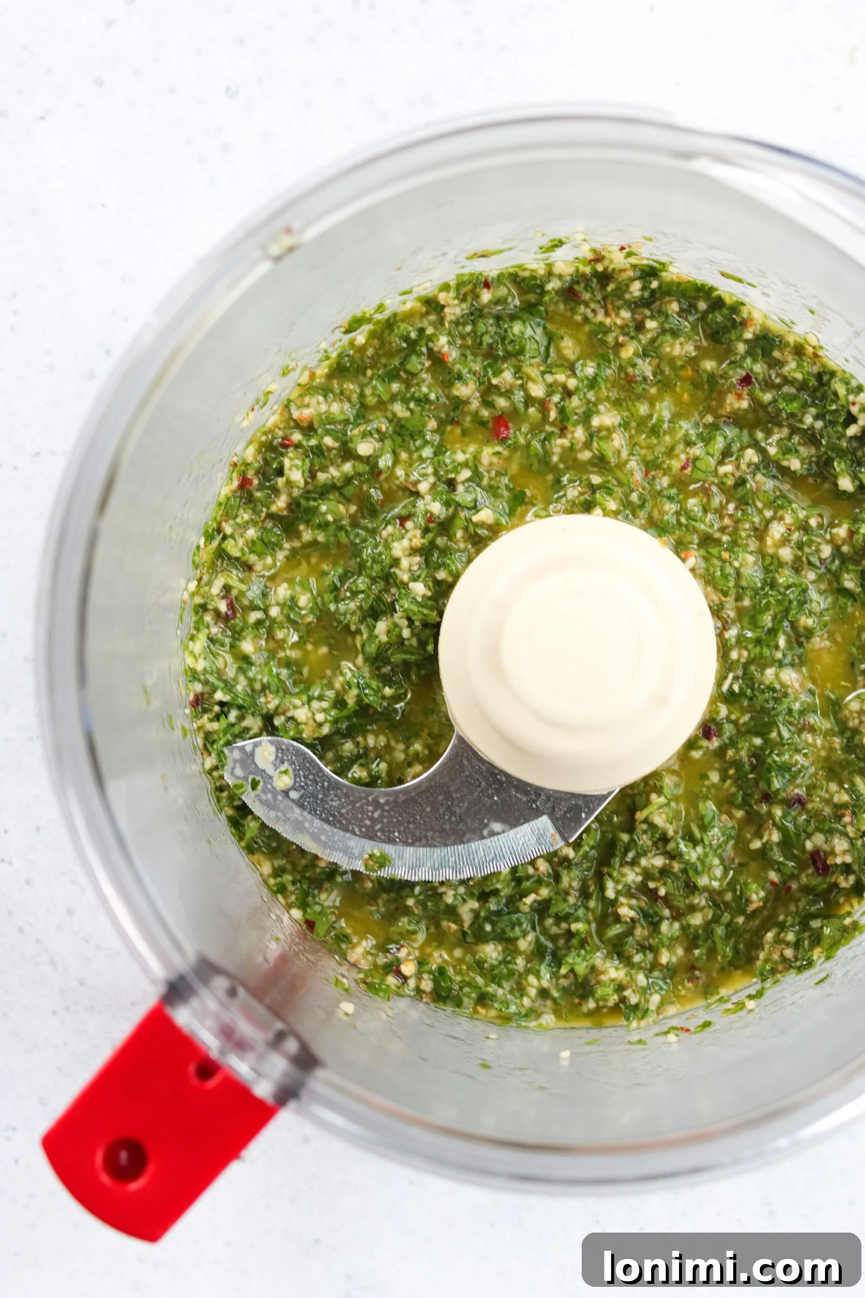 Close-up of a vibrant, chunky homemade chimichurri sauce in a glass bowl, garnished with a sprig of fresh parsley, ready to be served.