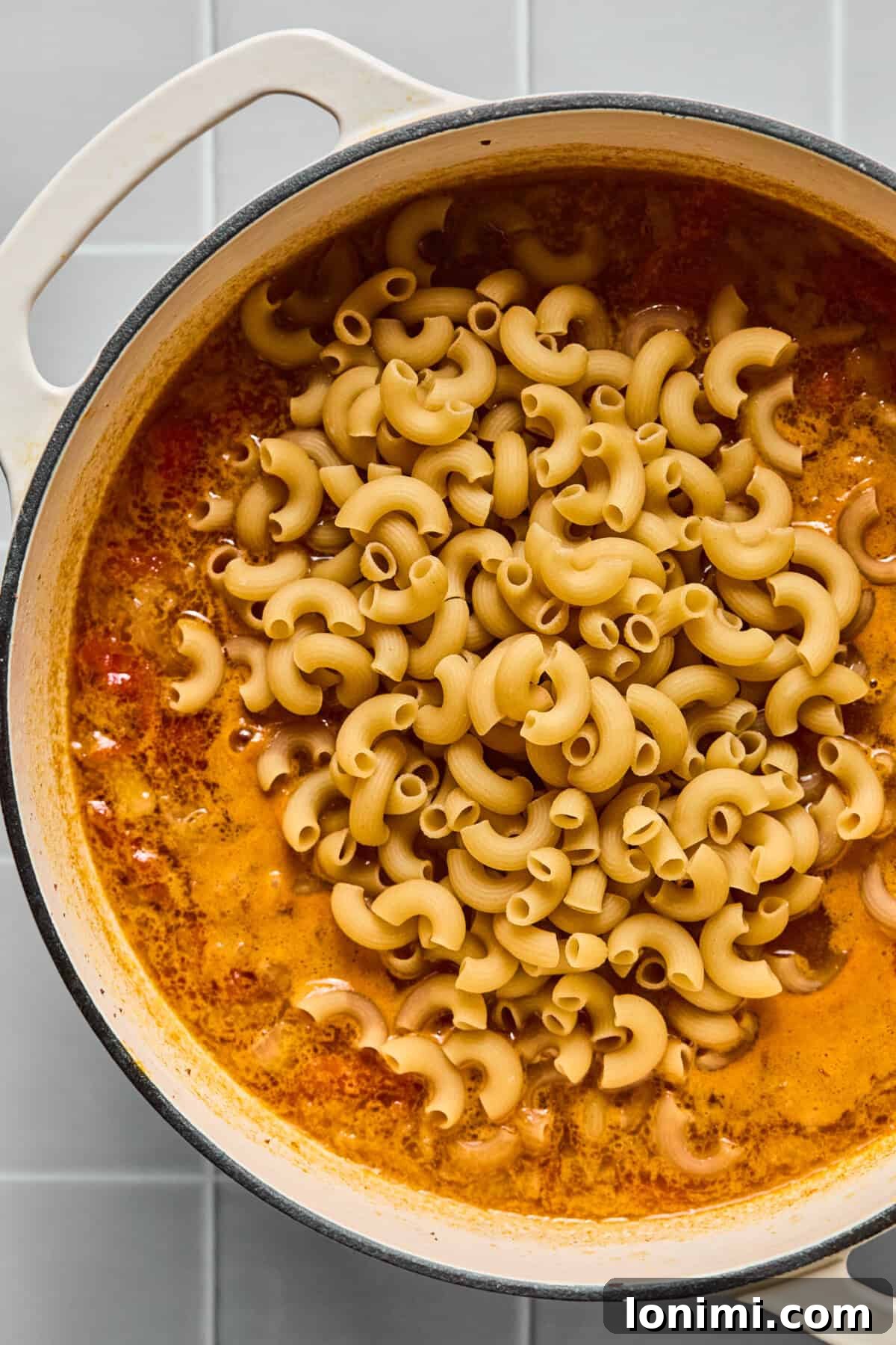Hearty Gluten-Free Beef and Pasta Skillet Dairy-Free Option 6 Gluten-free pasta, specifically elbow macaroni, being added to the simmering beef and broth mixture in a pot.