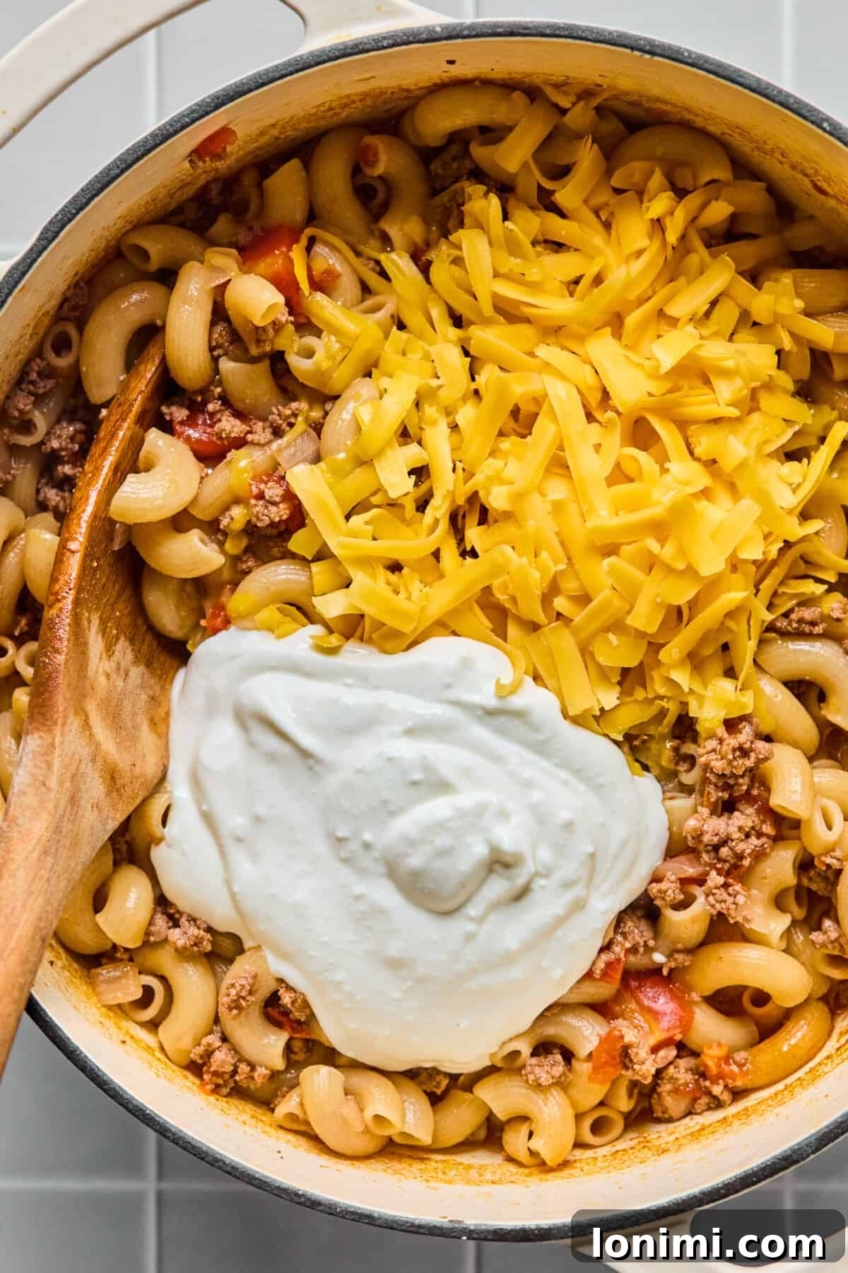 Hearty Gluten-Free Beef and Pasta Skillet Dairy-Free Option 8 Blended cottage cheese and shredded cheddar being stirred into the finished gluten-free hamburger helper in the pot, creating a creamy sauce.