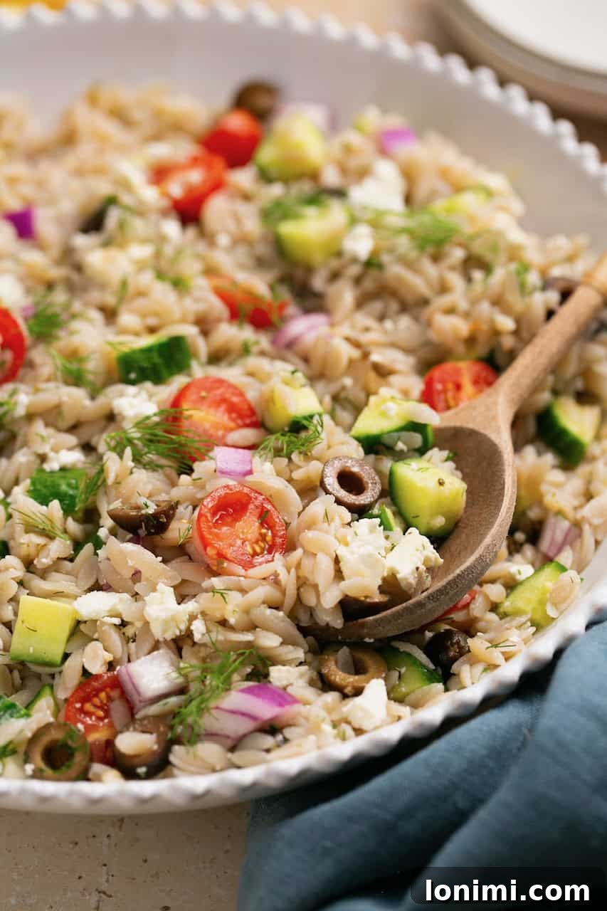A close-up view of the gluten-free Mediterranean orzo salad being scooped with a wooden spoon, highlighting the texture and fresh ingredients.
