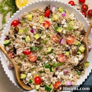 An appealing image of the finished gluten-free orzo Greek salad in a bowl with a wooden spoon
