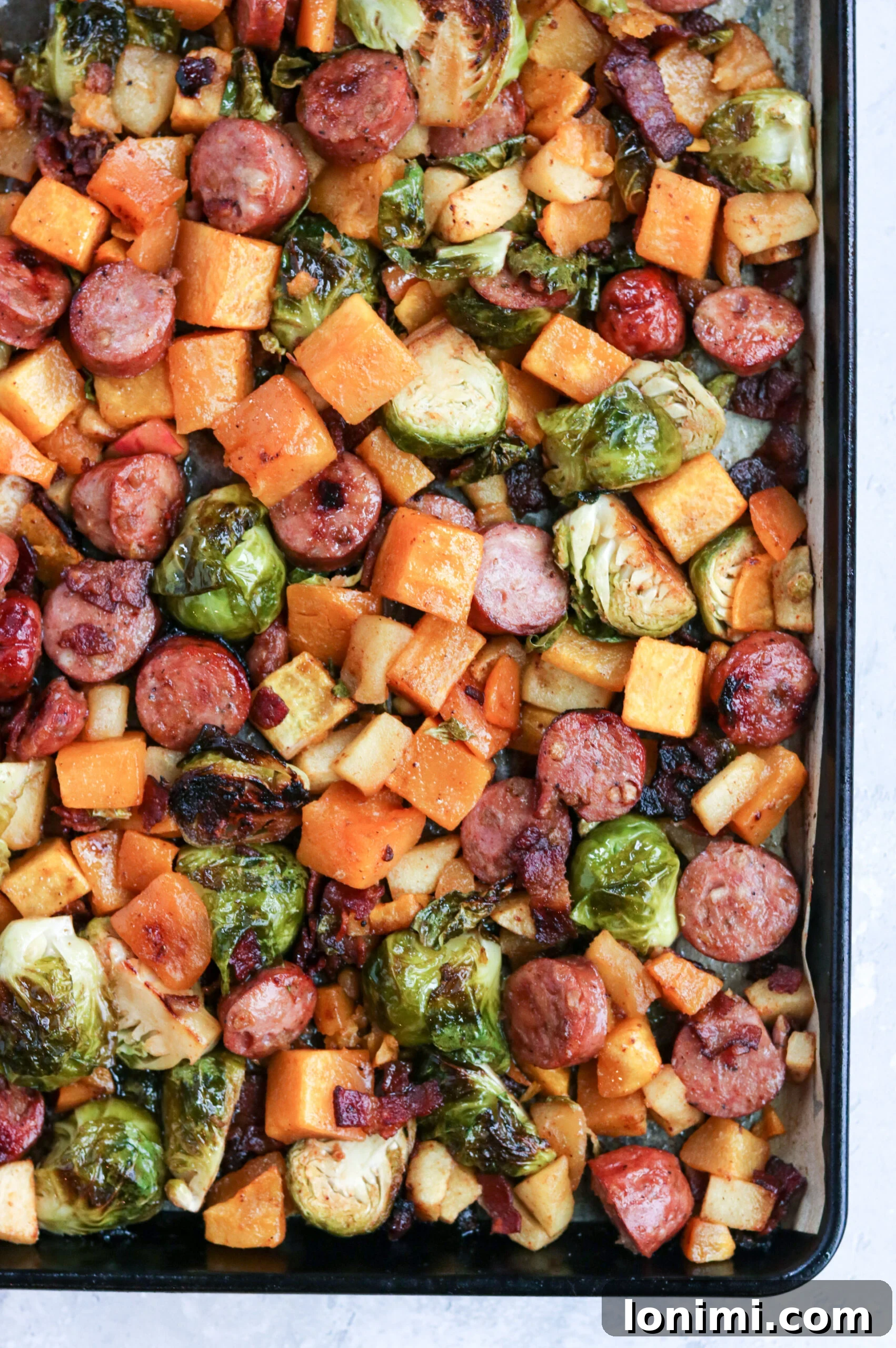 Whole30 Harvest Sheet Pan Dinner with chicken sausage, butternut squash, Brussels sprouts, apples, and bacon.