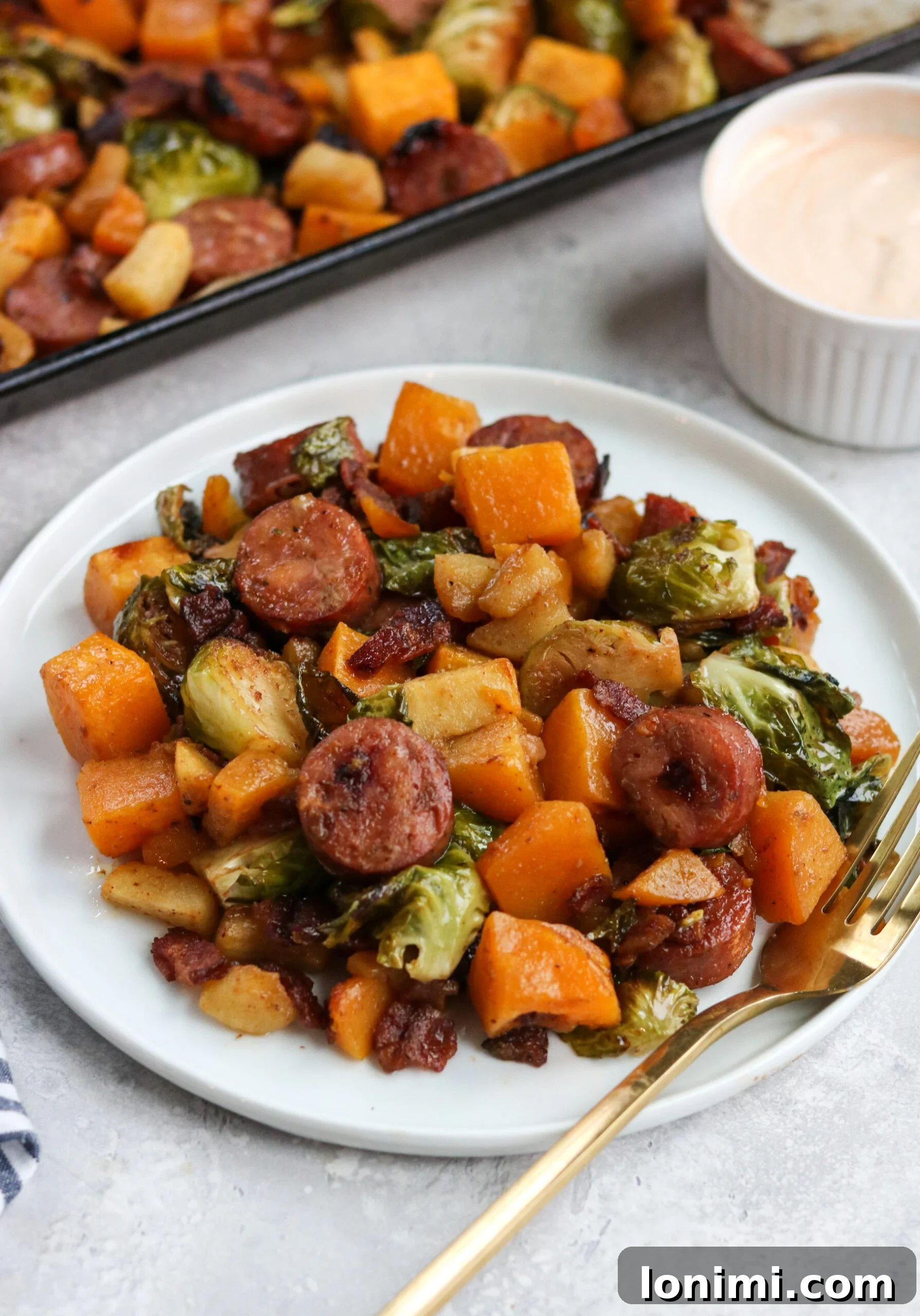 Close-up of roasted chicken sausage, butternut squash, Brussels sprouts, and bacon on a sheet pan.