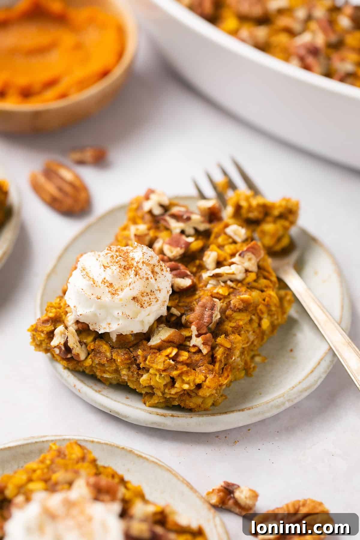 Spiced Pumpkin Oatmeal Bake 2 A perfectly baked pumpkin oatmeal slice on a plate, garnished with whipped cream and a fork, inviting a delightful fall breakfast experience.