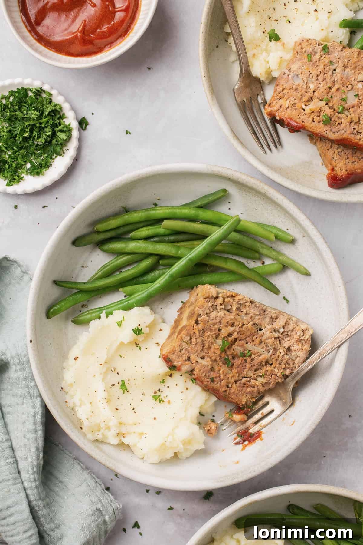 A well-plated dinner featuring a slice of gluten-free meatloaf, accompanied by green beans and mashed potatoes, with a fork ready to enjoy.