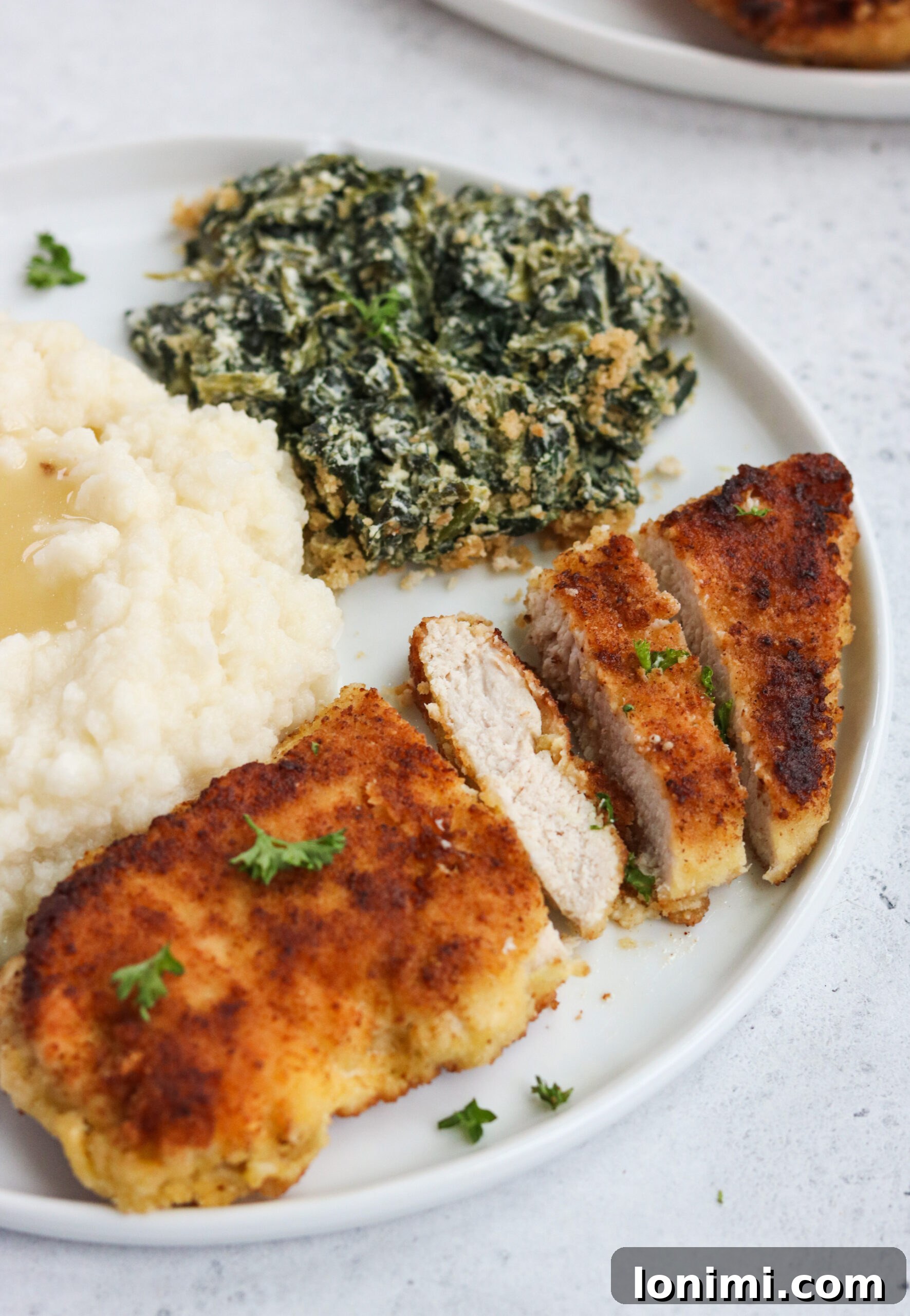 A serving of Whole30 Fried Chicken Cutlets with garlic mashed cauliflower and a creamy spinach casserole.