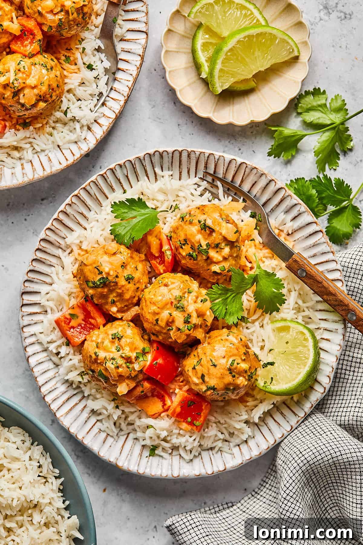 a serving of rice and thai turkey meatballs on a plate with a lime wedge and cilantro 