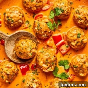 Thai Turkey Meatballs in red curry sauce in a skillet with a spoon lifting one of the meatballs