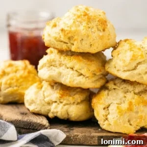 Fluffy gluten-free biscuits stacked on a cutting board, with jam in the background.