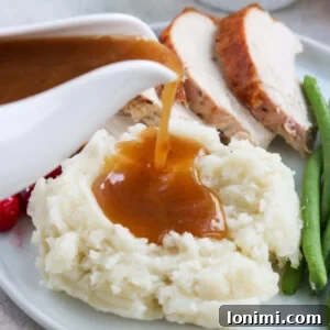 Rich Paleo gravy being poured over mashed potatoes, with roasted turkey in the background.