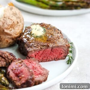Perfectly cooked air fryer filet mignon on a white plate, topped with a dollop of herb butter.