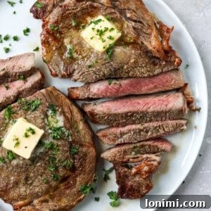 Sliced air fryer ribeye steak on a white plate, garnished with butter and parsley.