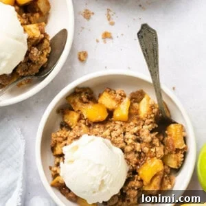 Warm apple crumble topped with a scoop of ice cream in a bowl, with a spoon digging in.