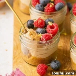 Individual no-bake mini cheesecakes in glass jars, topped with fresh berries, with a spoon taking a bite.