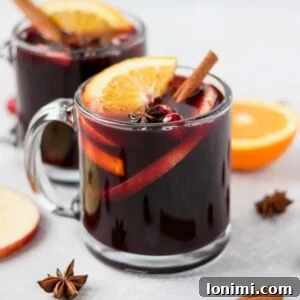 Steaming mulled wine in a glass mug, garnished with orange slices and cinnamon sticks.