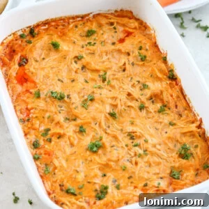 Healthy buffalo chicken dip in a white baking dish, garnished with parsley and served with carrots and celery.