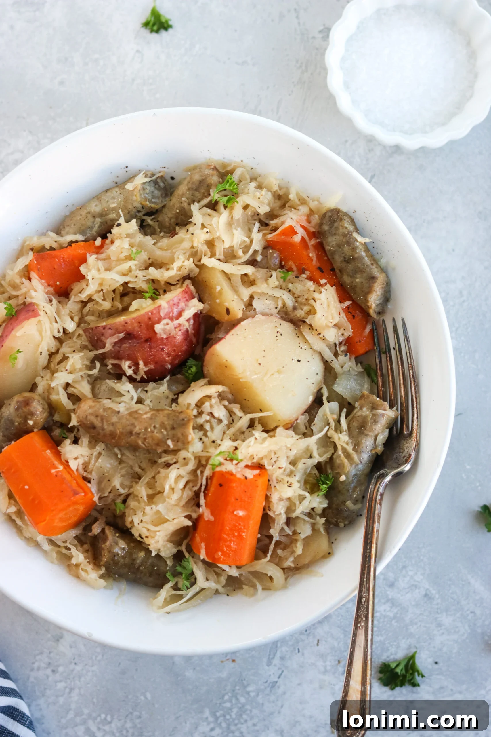 Slow Cooker Sweet and Savory Sausage with Apples and Sauerkraut 7 Finished Slow Cooker Sausage, Sauerkraut, and Apples in a serving bowl, garnished with fresh herbs.