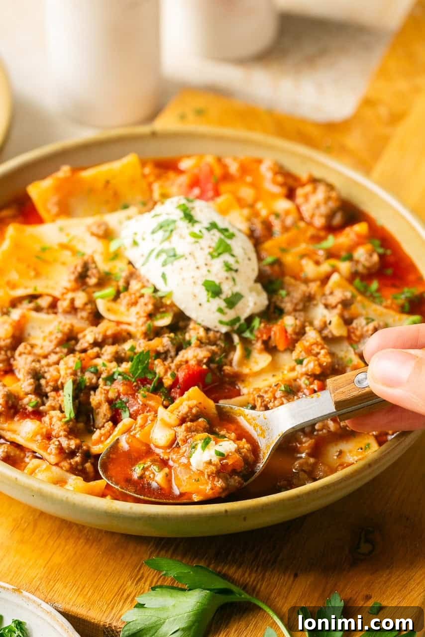 A spoon lifting a perfect bite of gluten-free lasagna soup, showcasing the noodles, meat, and rich broth.