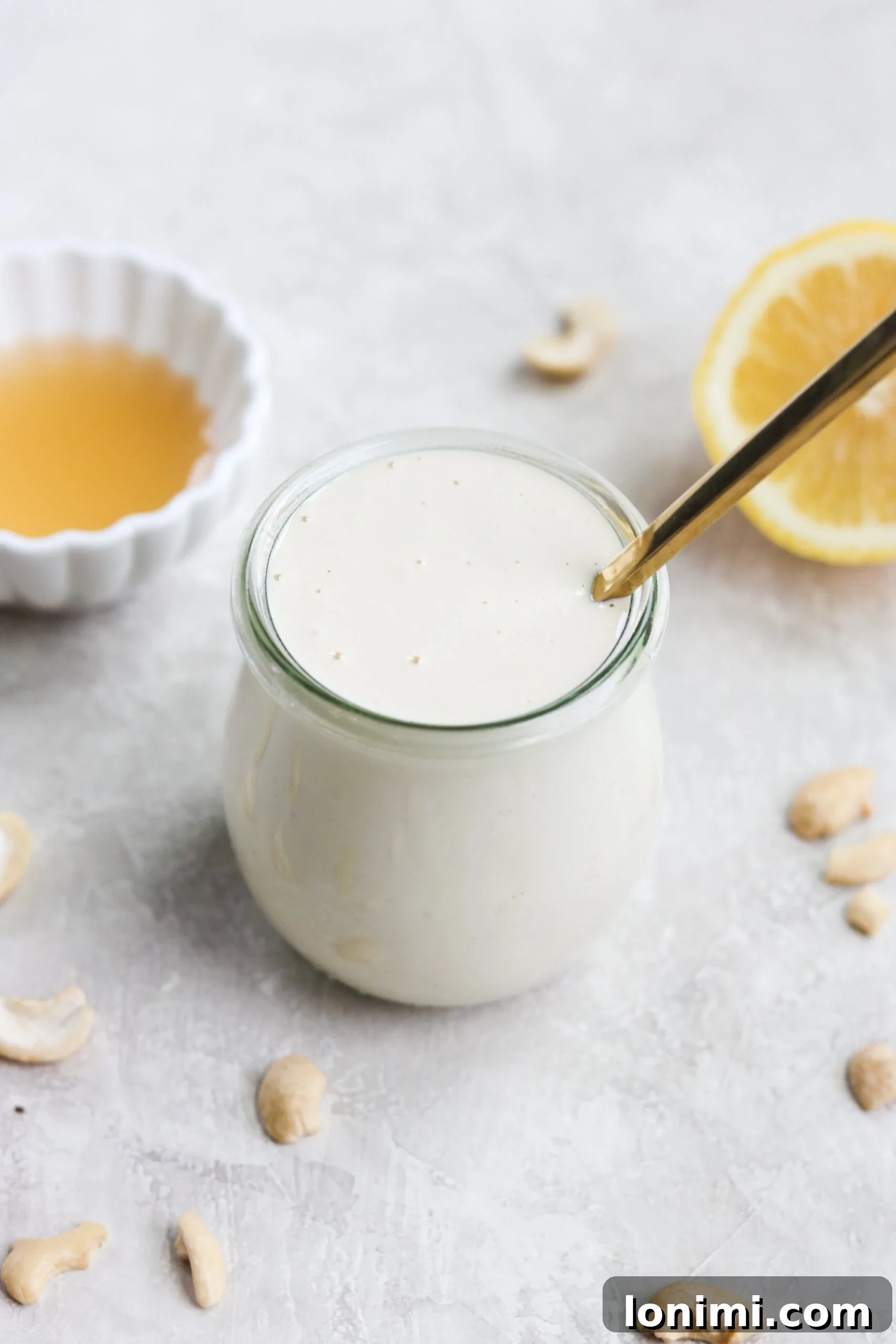 jar of dairy free sour cream with a gold spoon with cashews sprinkled on the surface next to a bowl of apple cider vinegar and half of a lemon