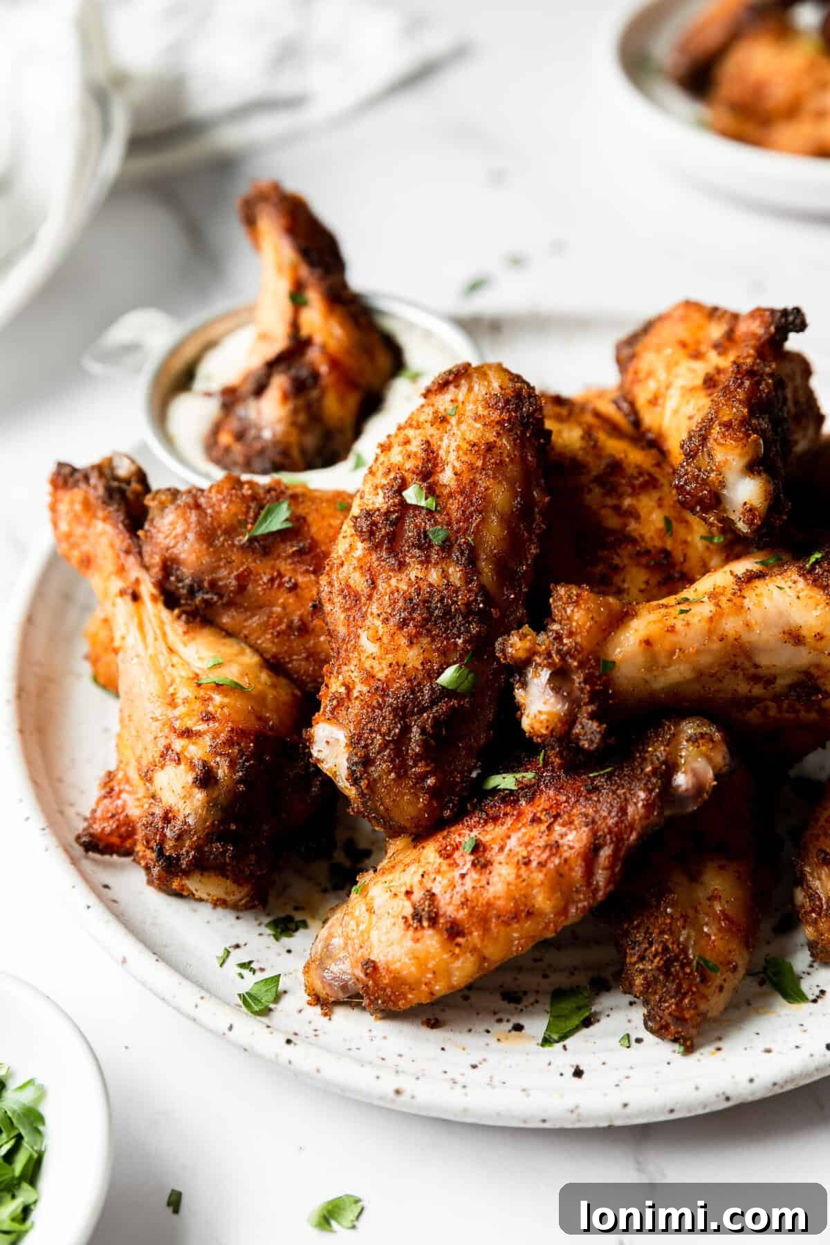 Close-up of baked chicken wings on a plate, one being dipped in ranch, emphasizing the crispy texture.