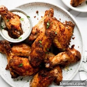 Crispy dry-rubbed baked chicken wings on a white plate with one being dipped in ranch dressing