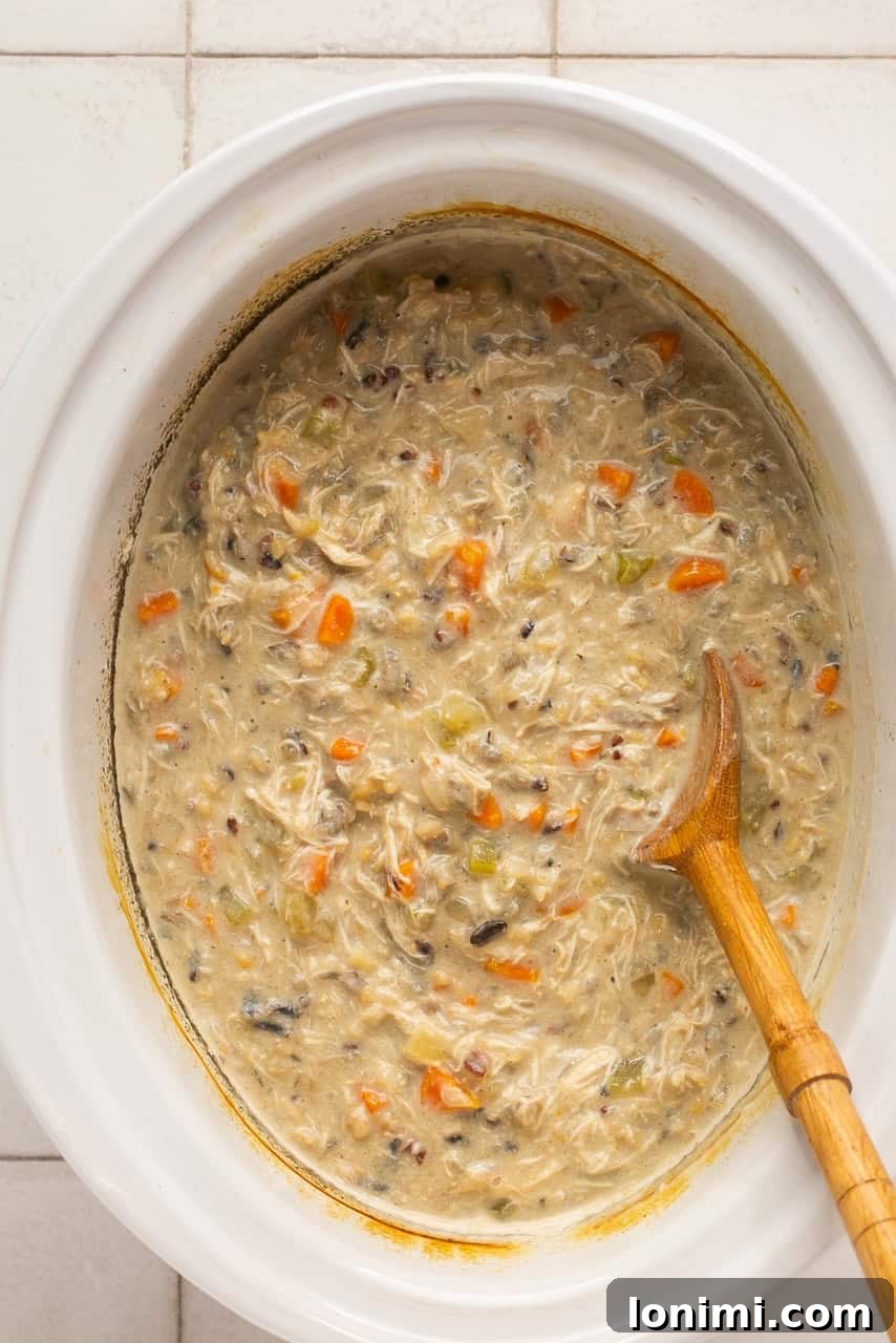Your Favorite Panera Chicken and Wild Rice Soup Made Gluten Free 6 Creamy, gluten-free Panera copycat chicken and wild rice soup simmering in a slow cooker, with a wooden spoon for stirring.