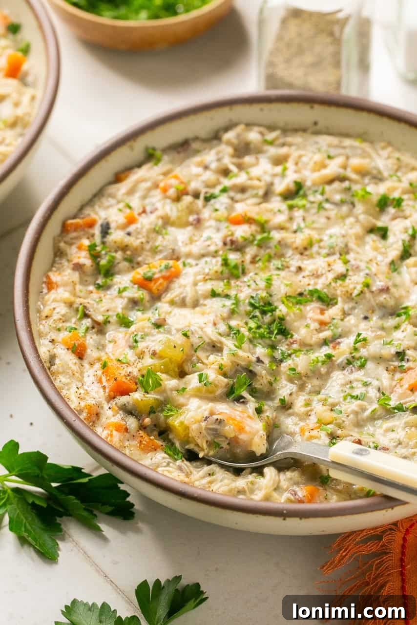 Your Favorite Panera Chicken and Wild Rice Soup Made Gluten Free 7 An up-close, appetizing shot of creamy chicken and wild rice soup in a bowl, generously topped with vibrant fresh parsley.