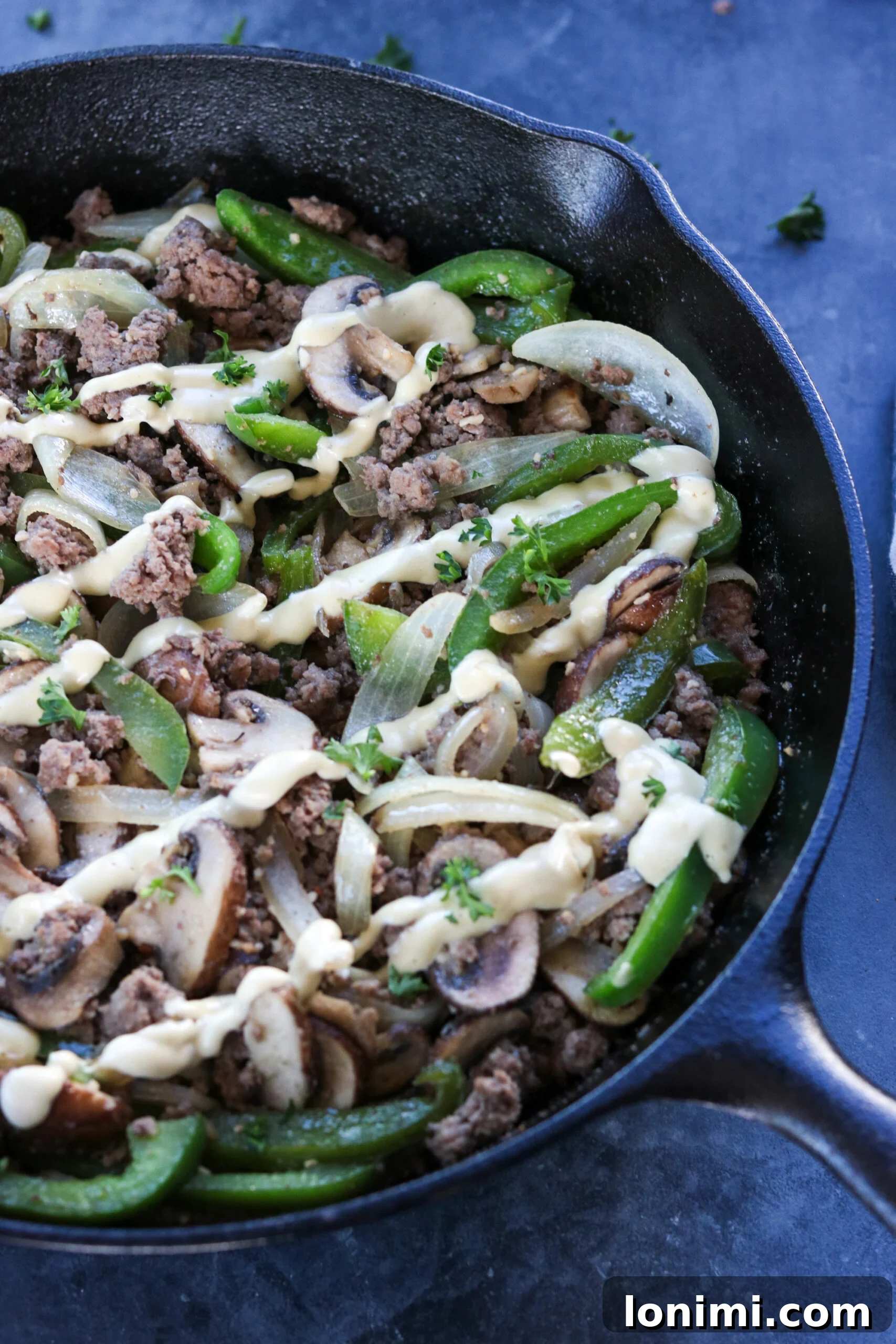 A high-angle shot of the Whole30 Philly Cheesesteak Skillet with the cashew cheese sauce generously drizzled over the top, ready to be served.