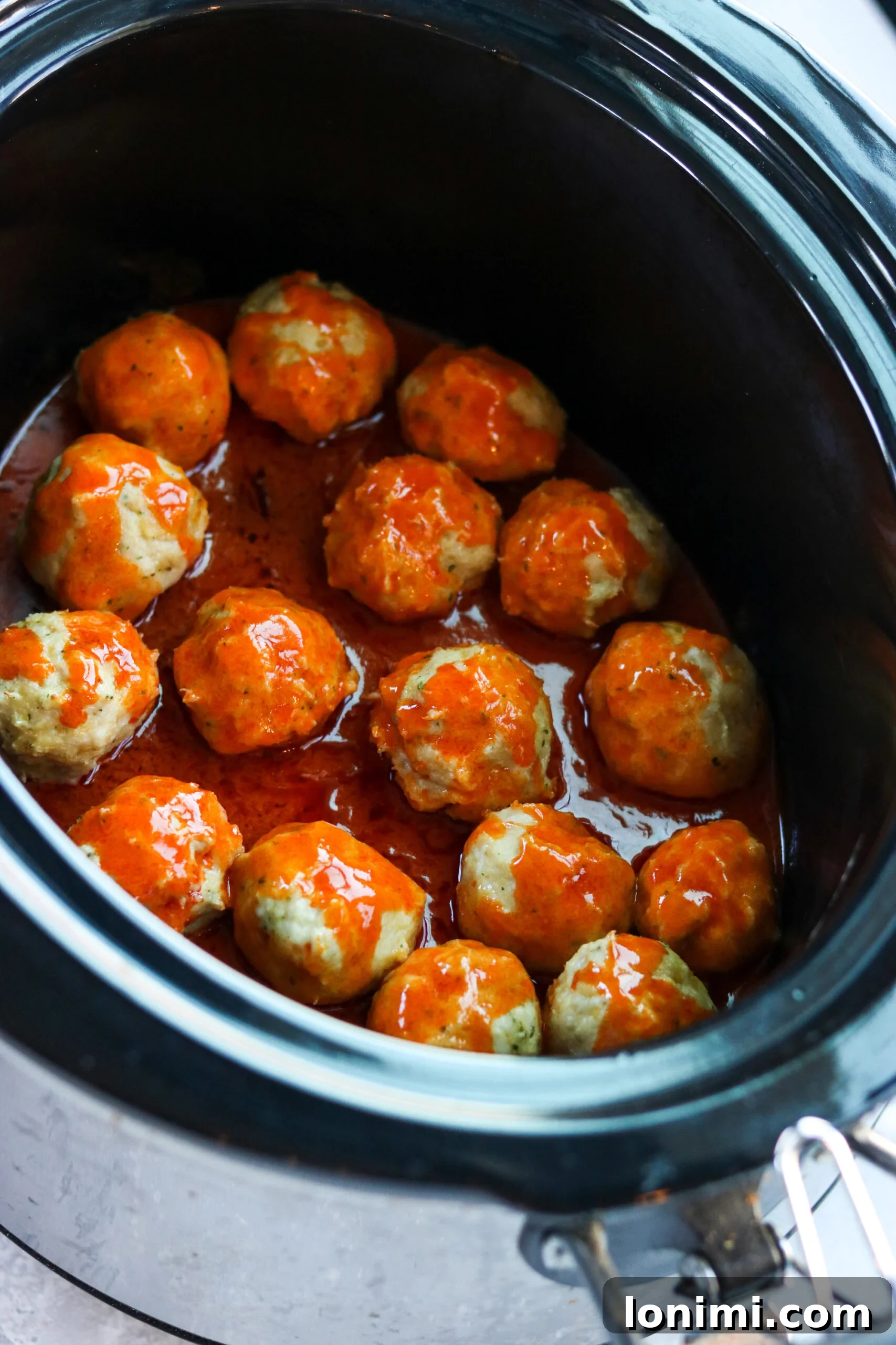 A slow cooker filled with buffalo chicken meatballs simmering in a rich, red sauce, ready to be served