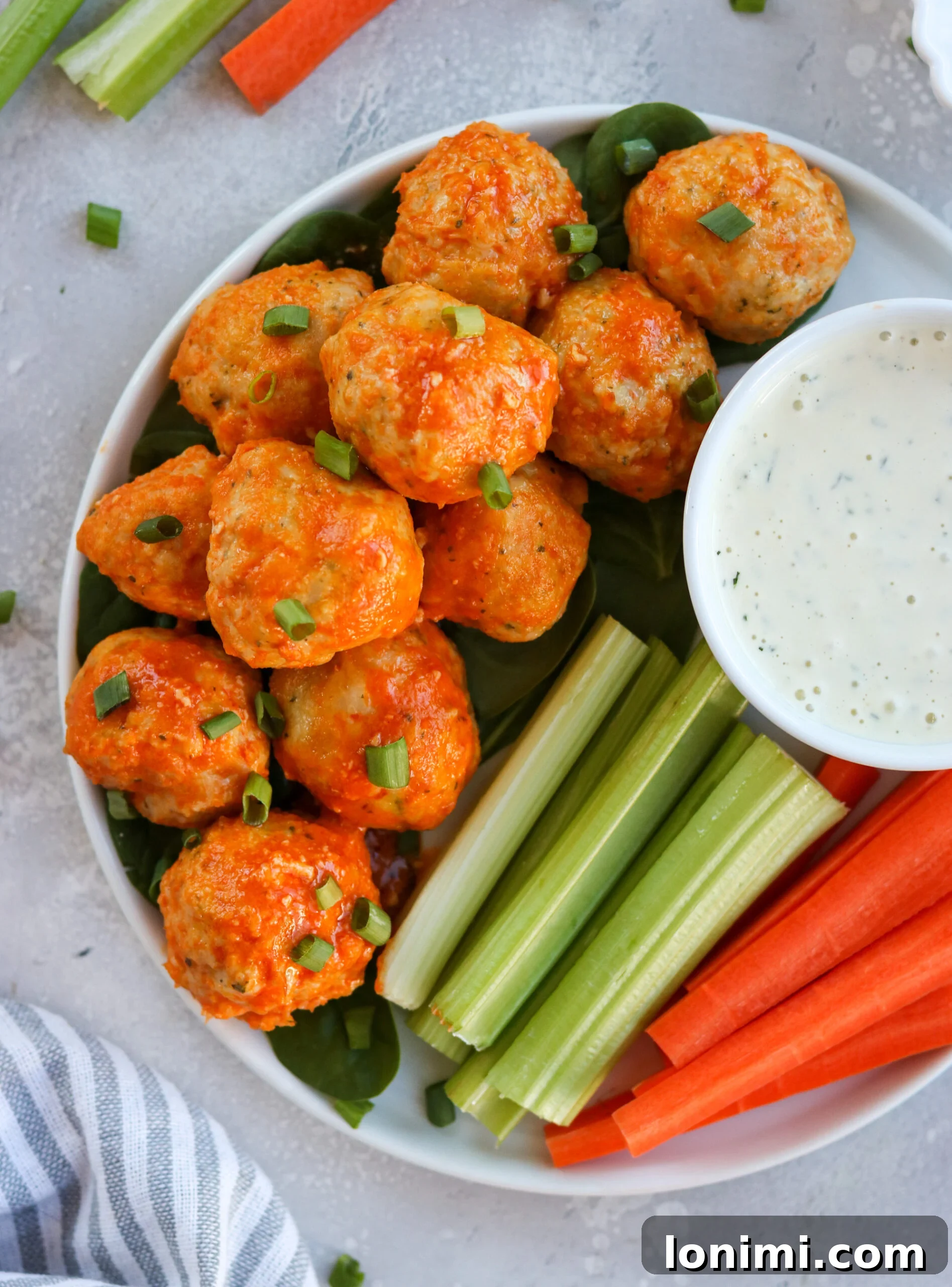 A vibrant bowl of buffalo chicken meatballs served with fresh avocado and other green vegetables, illustrating a full meal