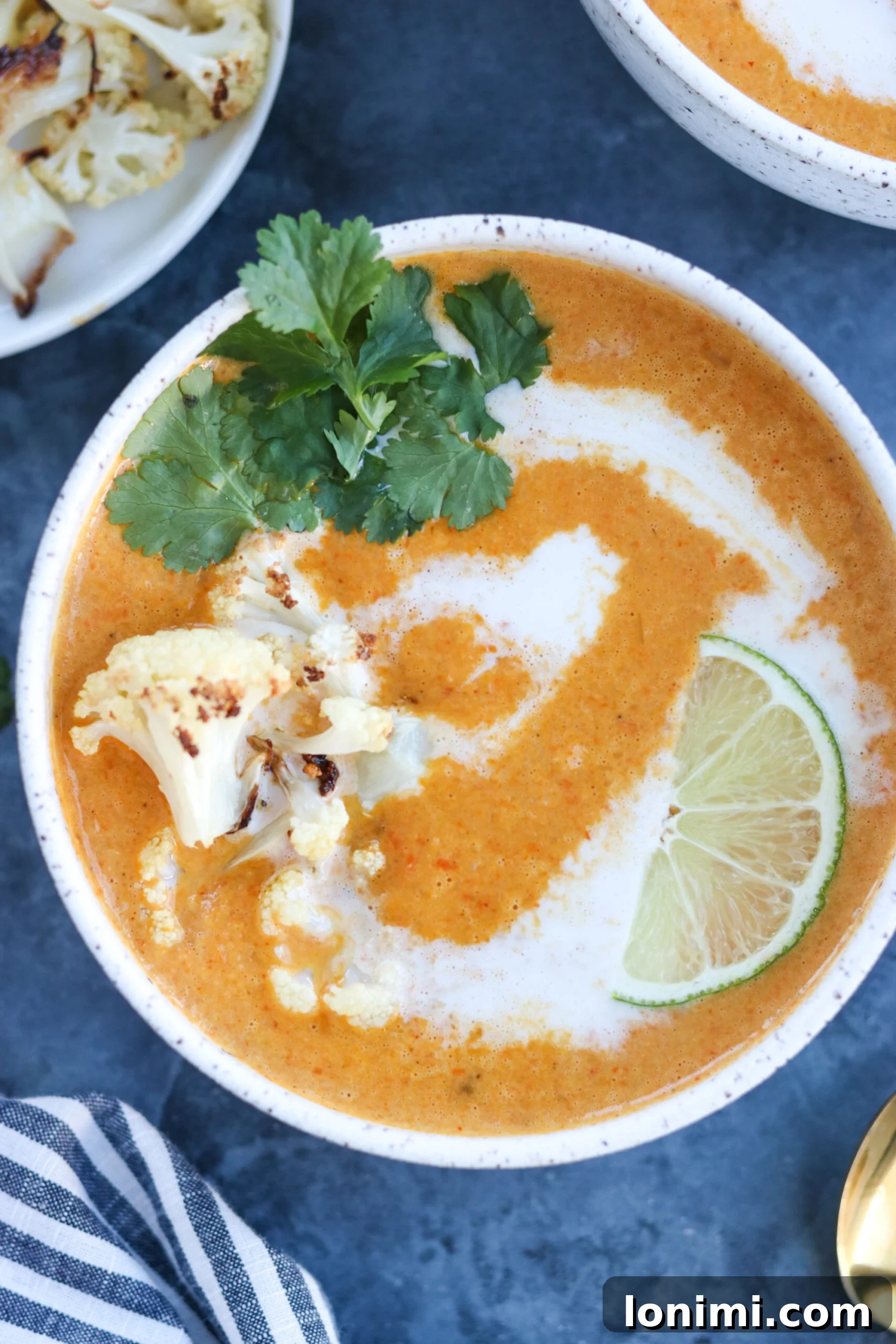 Creamy Curried Cauliflower Carrot Soup in a bowl, topped with a delicate swirl of coconut milk, fresh cilantro, and a lime slice.